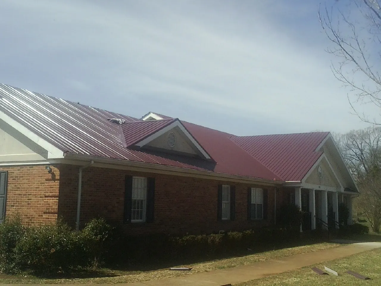 Red metal roof with gabled entries on a long brick building, from a Hail Damage Roof Repair job in Walthourville