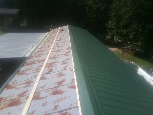 Old rusted panels beside newly installed green metal roofing — Wind Damage Roof Repair by Roofing Brothers in Walthourville