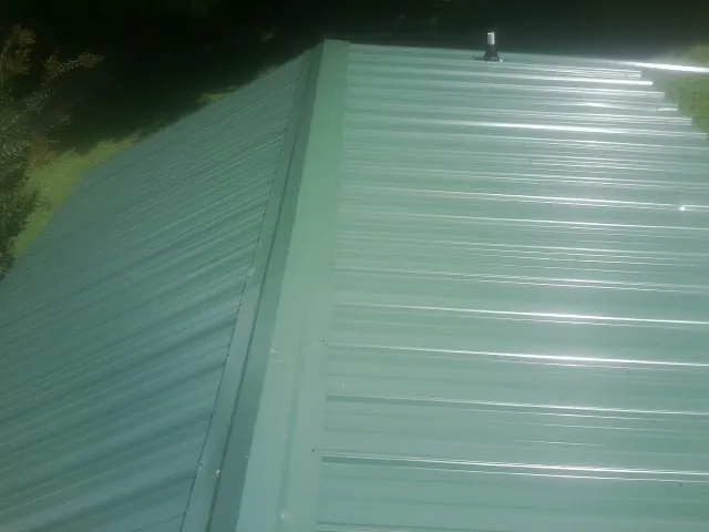 New green metal panels meeting at the ridge of a roof — Flat Roof Repair work by our crew in Walthourville