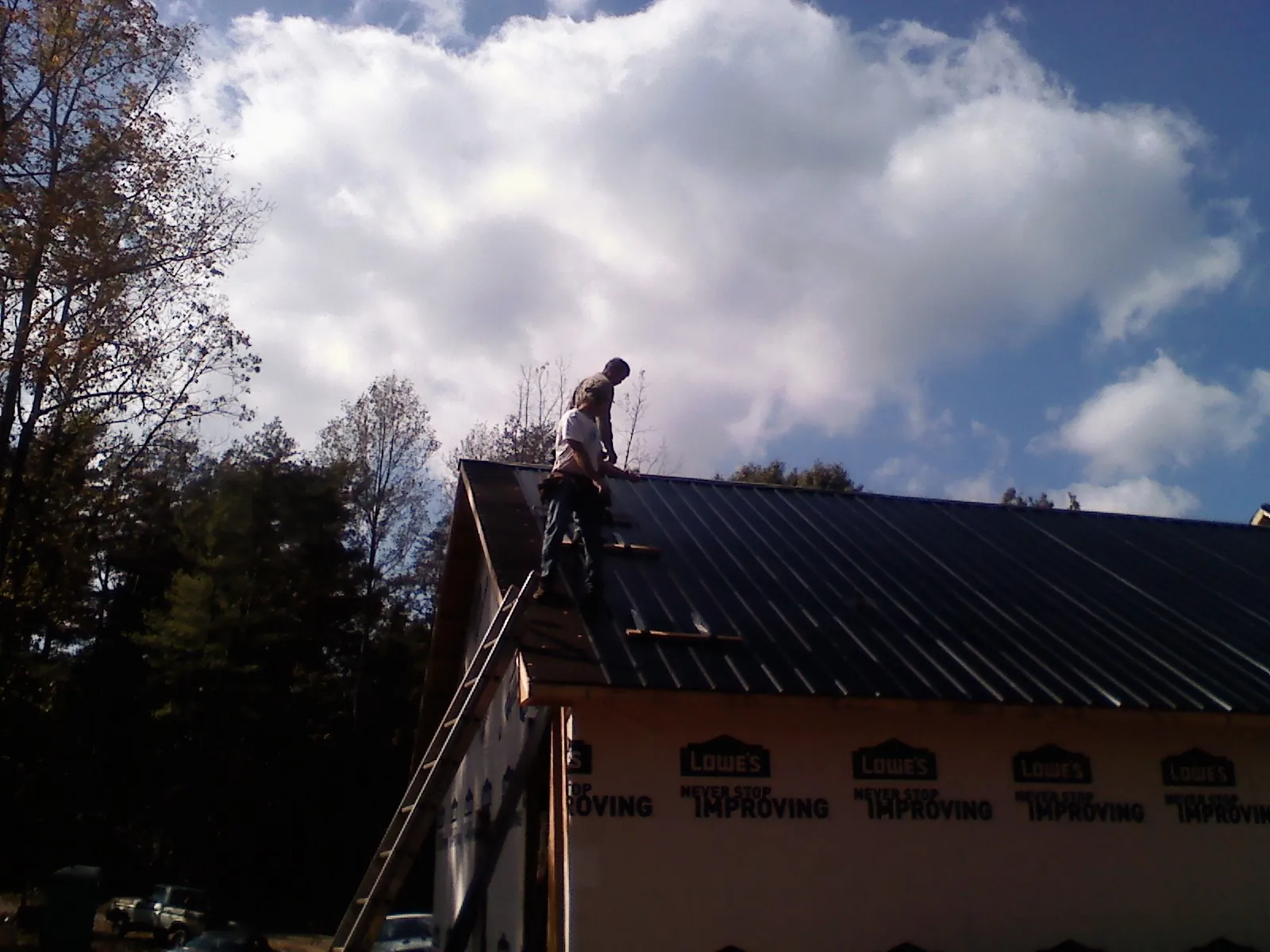 Roofer fastening dark metal panels high against a cloudy sky, from a Roof Inspection job in Walthourville