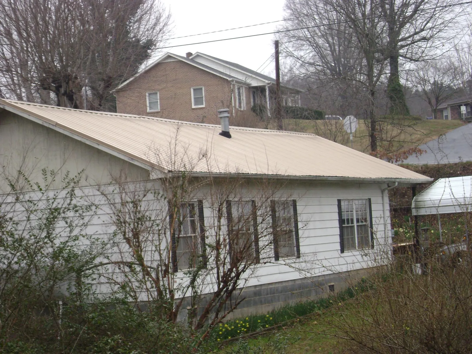 Tan metal roof on a white sided house set into a hillside — Commercial Roofing by Roofing Brothers in Walthourville